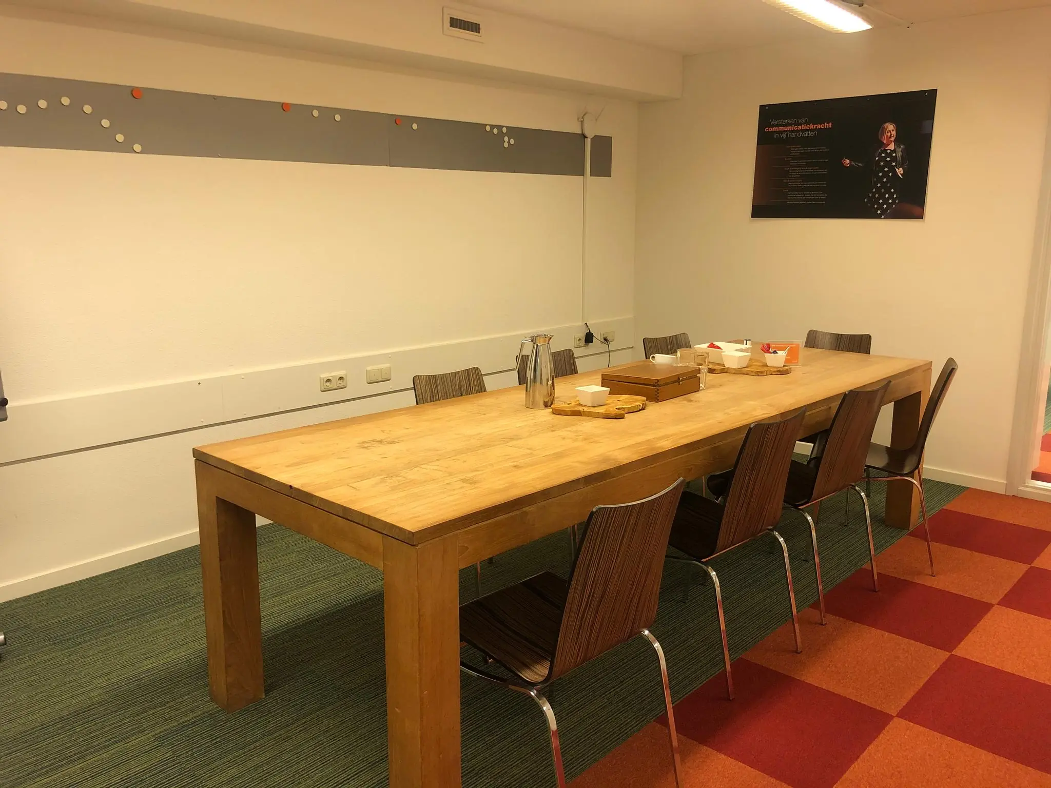 Vergaderruimte aan de Prins Hendrikkade met een lange houten tafel, zes stoelen en een presentatieposter aan de muur.